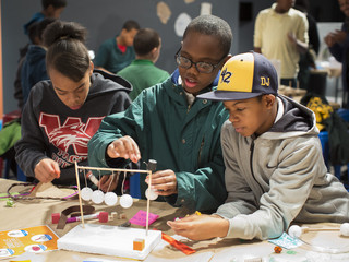 Three kids play with craft supplies to create their own Newton's cradle at the Black Creativity Innovation Gallery.