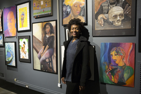 A visitor poses, smiling, in front of a wall of art at the 2017 Black Creativity Juried Art exhibit.