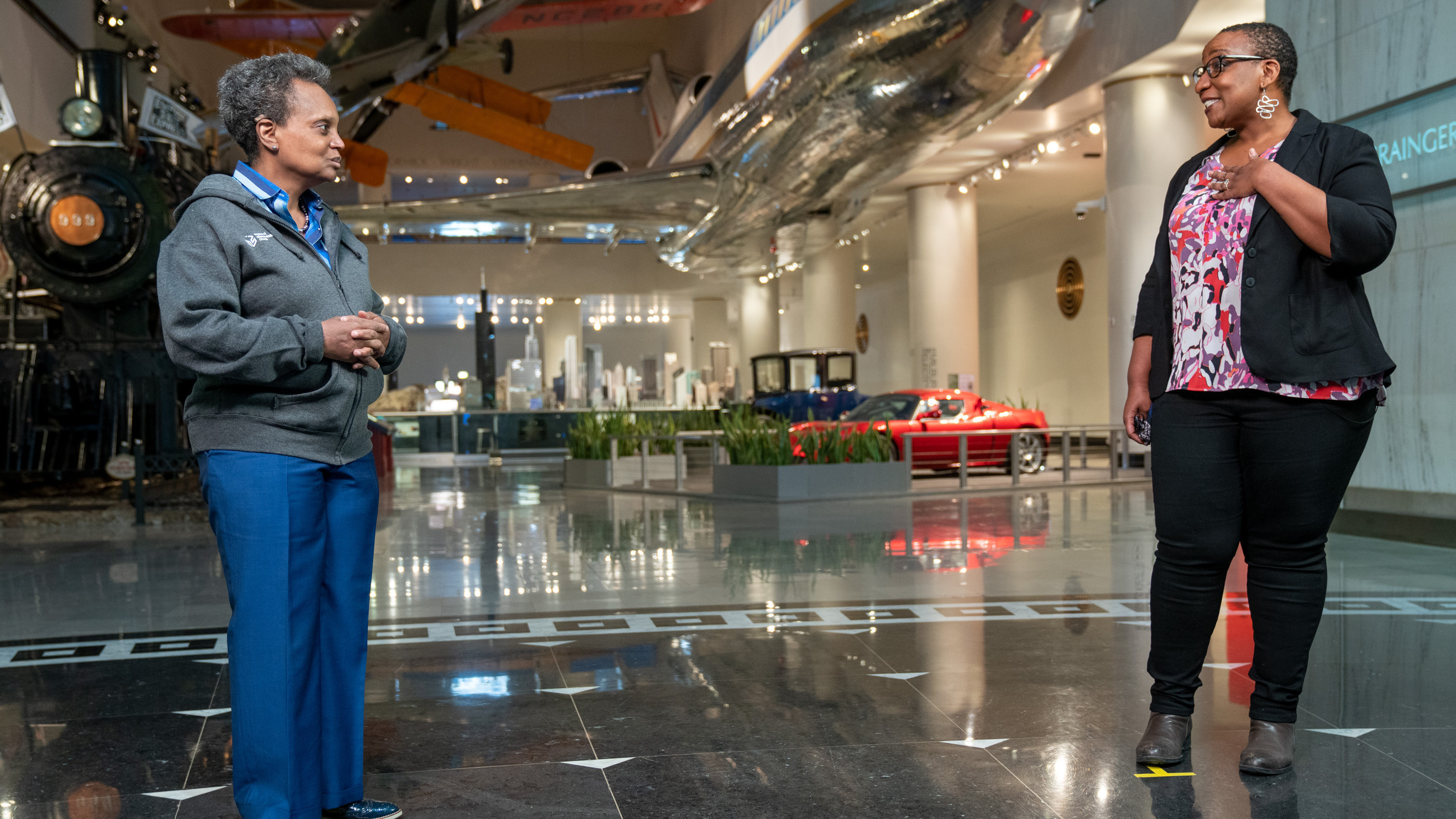Mayor Lori Lightfoot and a museum employee talk in front of the transportation gallery